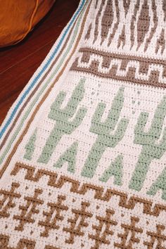 a crocheted blanket sitting on top of a wooden floor next to a pillow