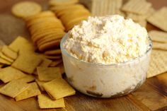 a bowl filled with cheese and crackers on top of a wooden table next to chips