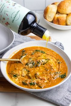 a white bowl filled with soup next to rolls and a bottle of wine on a table