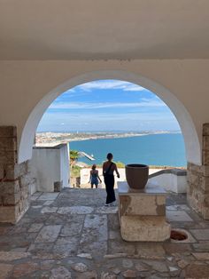 a woman and child are walking through an archway to the ocean in front of them