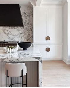 a kitchen with marble counter tops and white cabinets, along with two bar stools