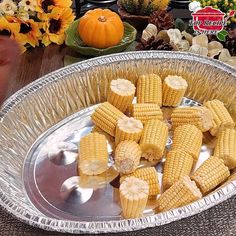 corn on the cob in a metal pan with flowers and pumpkins behind it