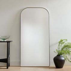 a large mirror sitting next to a black vase on top of a hard wood floor