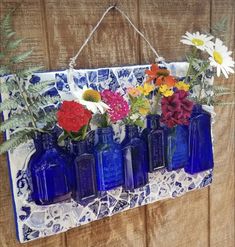 blue glass vases with flowers in them hanging on a wooden wall ornament