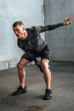 a man in black shirt and shorts doing squats with one hand on his hip