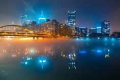 the city skyline is lit up at night with lights reflecting in the water and fog