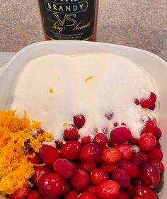 grapes and orange zest in a white bowl next to a bottle of brandy