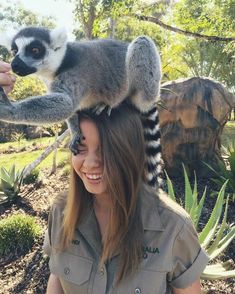 a woman wearing a hat with a lemura sitting on top of her head