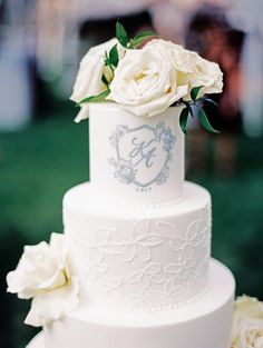 a three tiered white wedding cake with flowers on the top and initials on the side