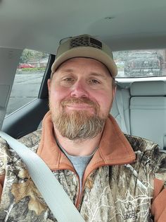 a man sitting in the back seat of a car wearing a camo jacket and hat