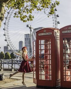 a woman in a red dress standing next to two telephone booths and a ferris wheel