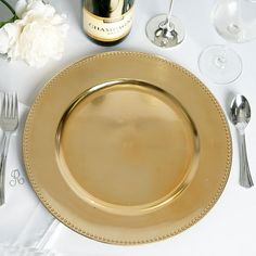 there is a gold plate on the table with silverware next to it and a bottle of wine