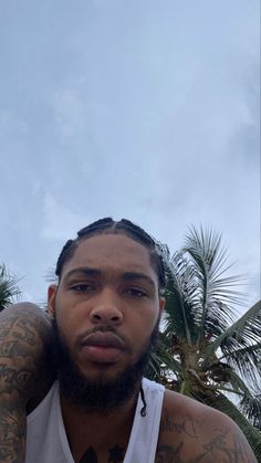 a man with tattoos on his arms and chest sitting in front of some palm trees