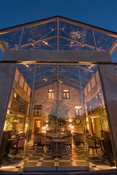 the inside of a glass walled building with tables and chairs in front of it at night