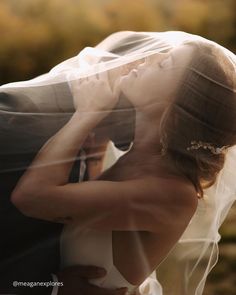 a bride and groom embracing each other under a veil on their wedding day in the sun