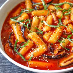 a white bowl filled with pasta covered in sauce and garnished with green leaves