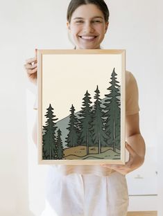 a woman holding up a painting with trees on it