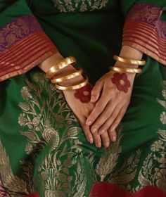 a woman's hands with gold bracelets on her wrist and green sari