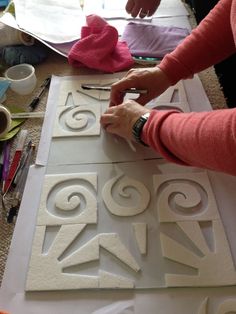 a woman is cutting out decorative designs on a piece of white paper with scissors and glue