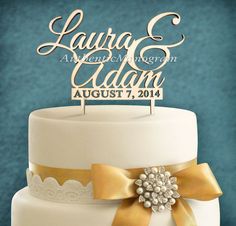 a white wedding cake with gold ribbons and a name sign that reads lauren & adam august 7, 2016