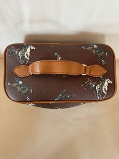 Must-have vanity/cosmetic bag for the traveling cowgirl! Beautiful faux brown leather with buckin' broncs artwork in white, brown and blue Fully-lined in brown fabric Durable and low maintenance Classy look and easy way to travel Simple zipper closure Gold colored hardware & light brown leather accents 4 rivets to protect when placed on hard surfaces Wide opening 9.4" x 6.7" x 5.1" 100% of the profits goes to the Bridle Up Hope charity whose mission is to inspire hope, confidence, & resilience i Brown Zipper Pouch Cosmetic Bag For Travel, Brown Pouch Cosmetic Bag For Travel, Brown Travel Pouch Cosmetic Bag, Brown Travel Cosmetic Pouch, Rectangular Brown Cosmetic Bag For Travel, Light Brown Leather, Brown And Blue, Leather Accents, Ways To Travel