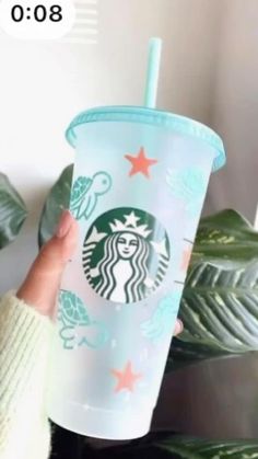 a person holding up a starbucks cup in front of a plant with stars on it