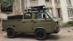 an army green truck parked in front of a run down building with no one inside