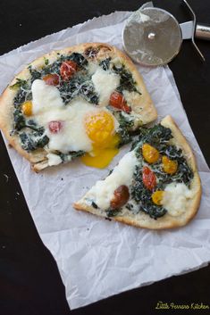 two pizzas with eggs and spinach on them sitting on wax paper next to a glass of water