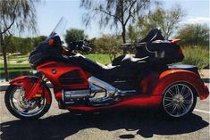 a red motorcycle parked in a parking lot next to a lake and trees on a sunny day