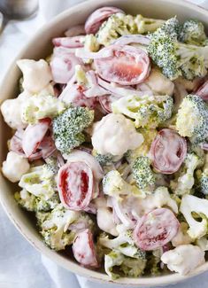 a bowl filled with broccoli, cauliflower and red onion salad next to a spoon