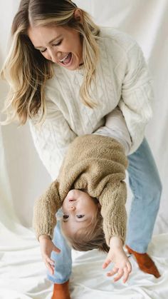 a woman is playing with a baby on her back while she holds him upside down