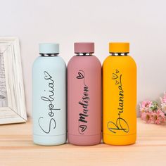 three different colored water bottles sitting next to each other on top of a wooden table