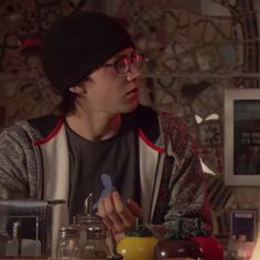 a young man sitting at a table in front of a candle and some food on the counter