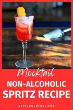 Pink colored cocktail in tall wine glass with ice and orange peel on wood table.