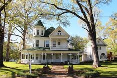 a large white house sitting in the middle of a lush green field with lots of trees