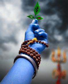 a person's hand holding up a green leaf with beads on it and a cross in the background