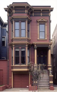 an old victorian style house with red siding and brown trim on the front door, stairs leading up to the second floor