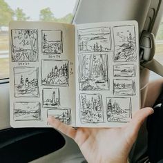 a hand holding an open book in front of a car window with drawings on it