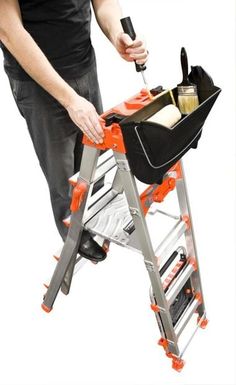 a man standing on top of a ladder holding a tool box and bottle in it