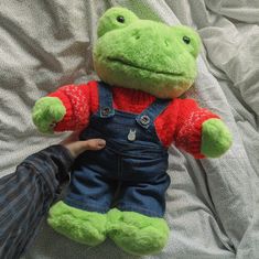 a person holding a green stuffed animal on top of a bed