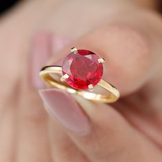 a close up of a person holding a ring with a red stone in the middle