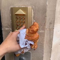 a hand holding a croissant wrapped in tissue next to a button on a wall