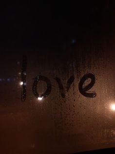 the word love written in wet glass on a rainy window sill at night time