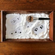 a wooden table topped with white frosting and animal footprints next to a makeup brush