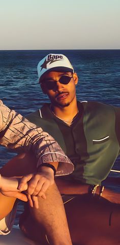 a man sitting on the back of a boat next to another man wearing sunglasses and a hat