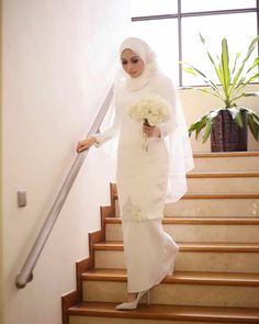 a woman in a white hijab is walking down the stairs with her bouquet