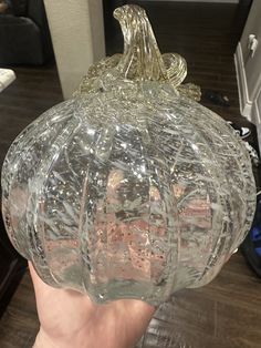 a hand holding a glass pumpkin on top of a table