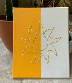 a yellow and white canvas with an embroidered sun design on it next to a potted cactus