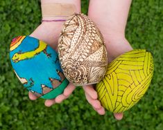 two hands holding three different colored eggs