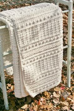 a white blanket sitting on top of a chair next to leaves in the grass and fallen leaves